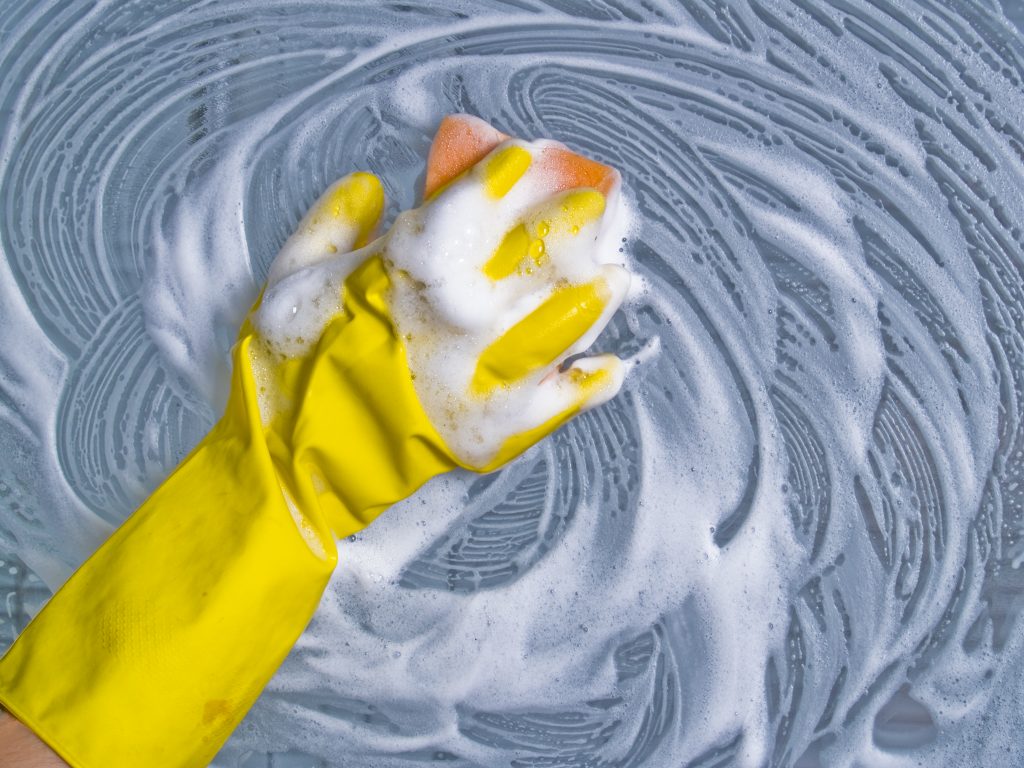 hand in yellow glove cleaning window with soap and orange scrub with Cleaning with Krystal in Palm Beach